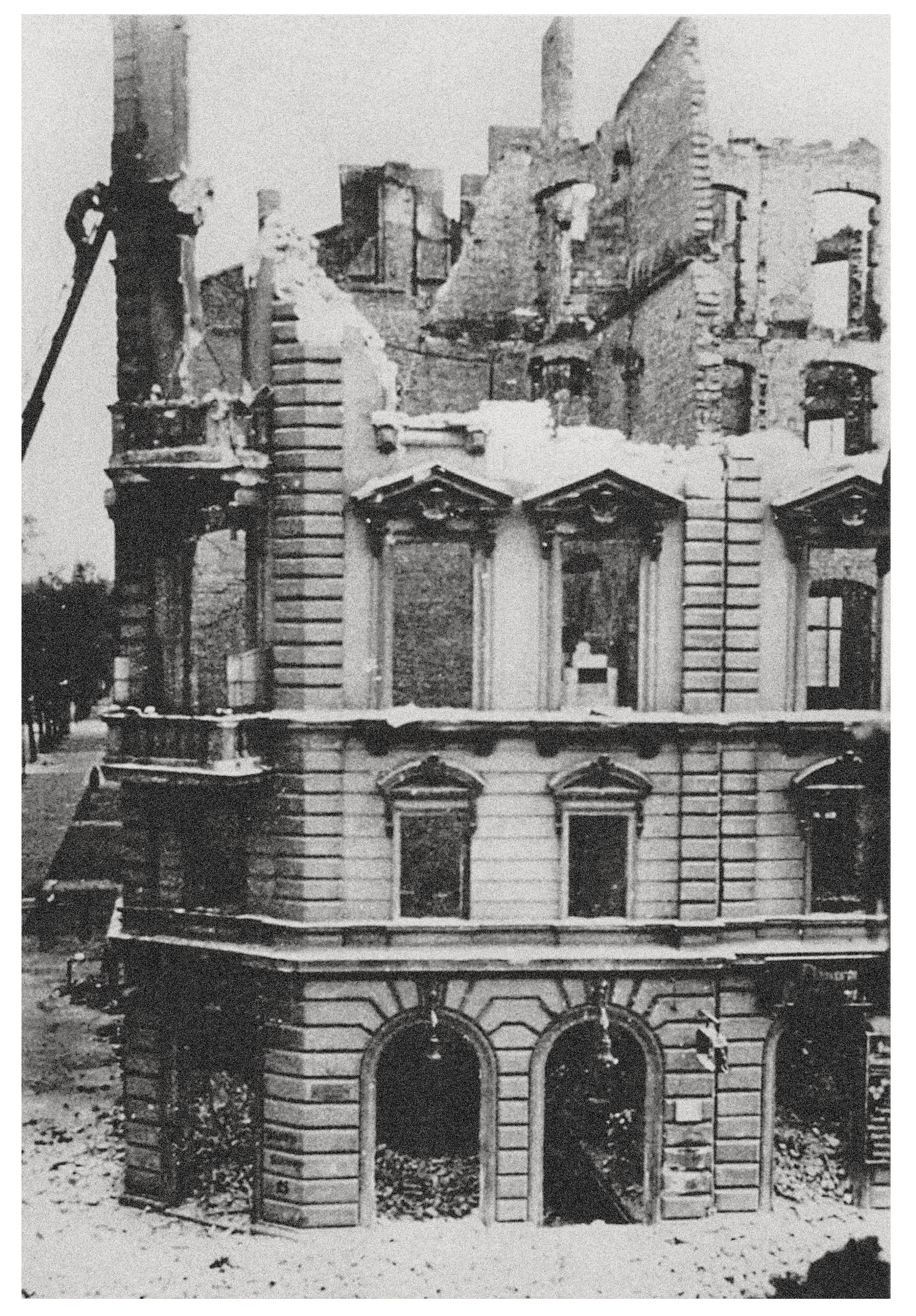 Dieses Schwarz-Weiß-Foto zeigt die zerbombte Ruine eines prachtvollen, mehrstöckigen Gebäudes mit klassizistischer Fassade, von dem nur noch die Außenmauern stehen. Die Fensterhöhlen sind leer, das Dach fehlt komplett und im Inneren sind die Decken eingestürzt, sodass man durch die Fassade in den freien Himmel blickt. Am Boden liegen Berge von Trümmern vor den erhaltenen Rundbogen-Eingängen im Erdgeschoss.