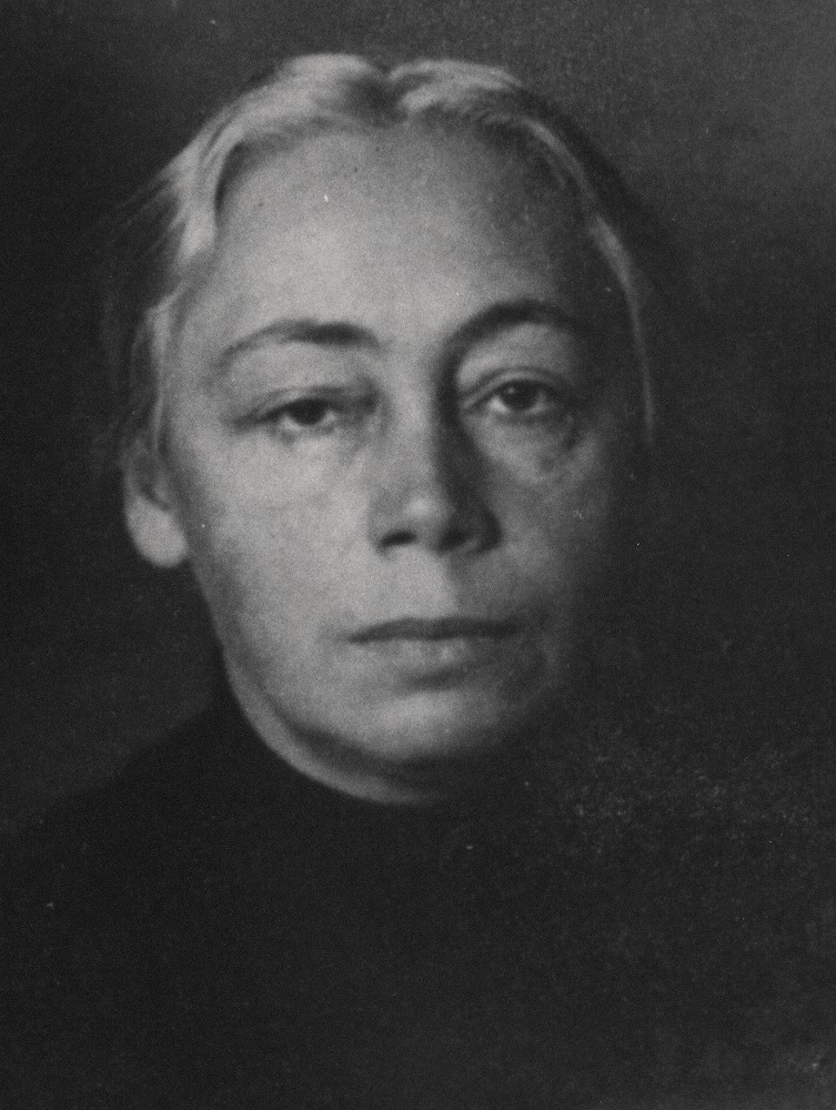 Ein Schwarz-Weiß-Foto zeigt das Gesicht von Käthe Kollwitz in einer nahen Frontalaufnahme vor einem dunklen, schlichten Hintergrund. Es entstand um 1914/15, nach dem Tod ihres Sohnes Peter. Fotograf:in unbekannt. Ihr helles, graues Haar ist streng mit einem Mittelscheitel nach hinten gekämmt, was ihre hohe Stirn und die klaren Gesichtszüge betont. Sie blickt mit einem ernsten, lebenserfahrenen Ausdruck direkt in die Kamera. Ihr Blick wirkt müde und niedergeschlagen. 
Dieses Bild, ein Detail aus einem Porträt mit ihrem Sohn Hans, befindet sich im Nachlass der Künstlerin im Archiv des Kollwitz Museum Köln, Inv.: Nr. F 01.b-07.
