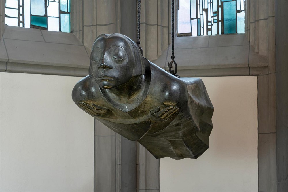 Die Aufnahme des Fotografen Chris Franken zeigt die Bronzeplastik »Der Schwebende« von Ernst Barlach, den Zweitguss nach dem Original-Werkmodell von 1939 an seinem heutigen Ort in der Kölner Antoniterkirche, frontal nach links gewandt. Die lebensgroße, waagerecht schwebende Bronzefigur hängt an zwei Ketten frei in der Luft, wobei ihr gerader Körper und die vor der Brust gekreuzten Arme eine tiefe Ruhe ausstrahlen. Das Gesicht der Skulptur hat geschlossene Augen und wirkt wie insich versunken, während die fließende Form des Gewandes den Eindruck eines sanften Fluges verstärkt.