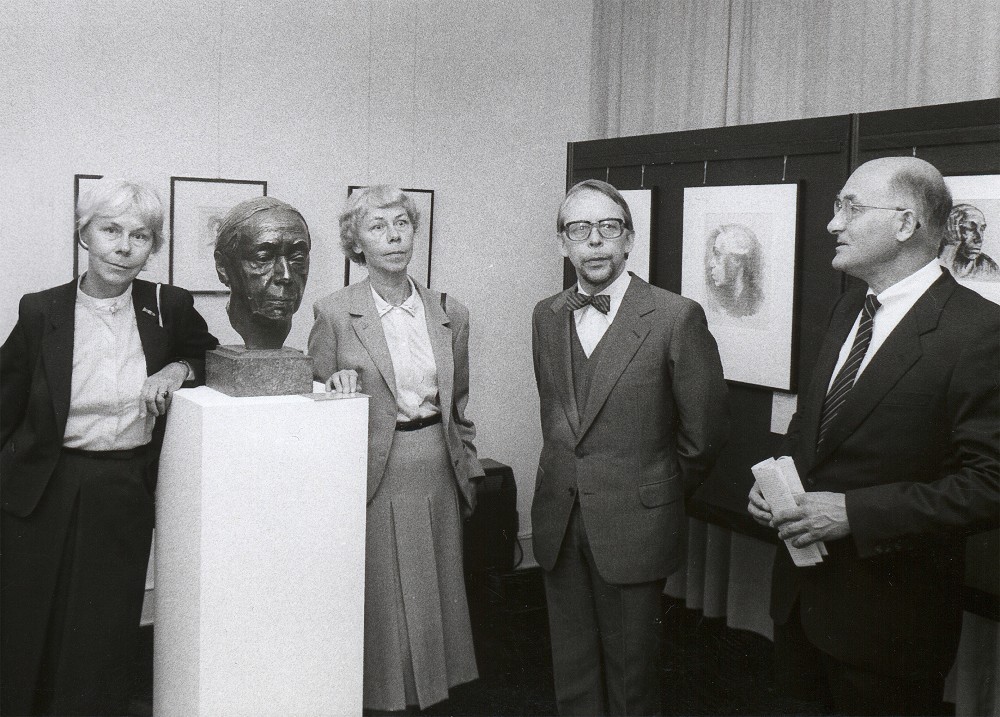 Das Schwarz-Weiß-Foto zeigt stehend die Kollwitz-Enkel Jutta Bohnke-Kollwitz, Jördis Erdmann, Arne Andreas Kollwitz und Hans-Joachim Möhle, Vorstandsvorsitzender der Kreissparkasse Köln (v.l.) bei der Eröffnung des Kollwitz Museum Köln 1985. Zwischen den Enkelinnen das Selbstbildnis in Bronze der Künstlerin, im Hintergrund weitere Werke.