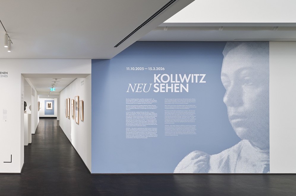 Das Foto zeigt die Schauwand im Museumsfoyer des Kollwitz Museum Köln mit dem Titel der Ausstellung KOLLWITZ NEU SEHEN in weißer Schrift auf blauem Hintergrund. 