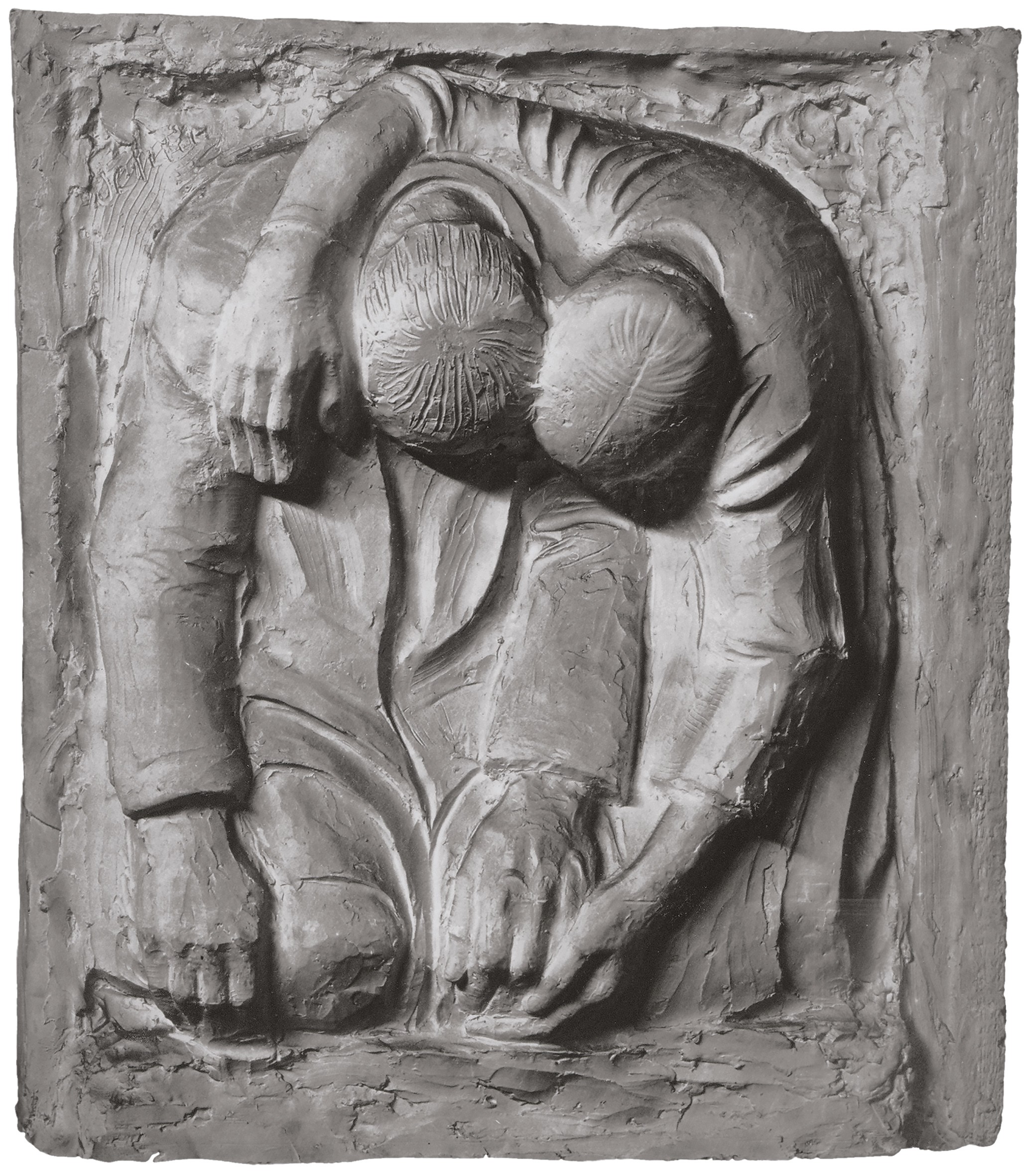 Das schwarz-weiß-Bild zeigt ein Gipsrelief mit zwei tief gebeugten Figuren, die sich in schwerem Kummer eng aneinanderdrücken. Ein Arm liegt schützend über der Schulter des Partners, während ihre beiden Köpfe kraftlos nach vorne sinken und sich berühren. Die raue, blockhafte Struktur der Oberflächen verstärkt den Eindruck von tiefer Trauer und gegenseitigem Halt.